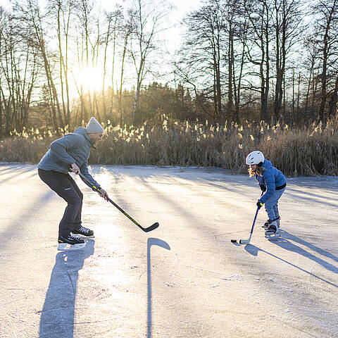 Erwachsener und Kind spielen am Flatschacher See Eishockey
