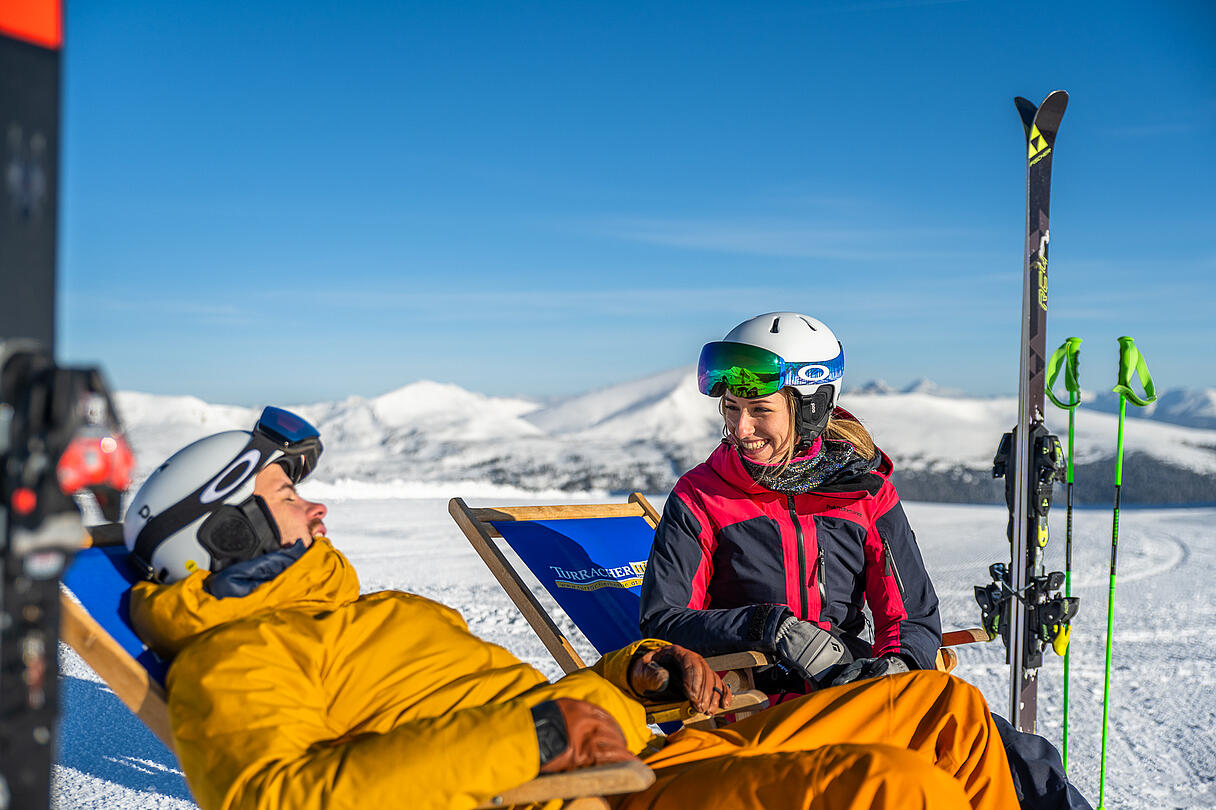 2 Personen sitzen in Liegestühlen, genießen die Sonne und haben Spaß miteinander