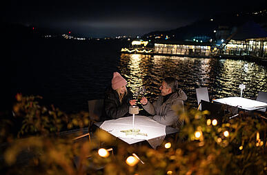 Pärchen sitzt am Abend direkt am Millstätter See bei einem Glas Wein im Advent
