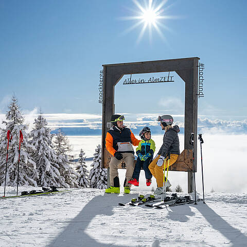 Familie mit Skiausrüstung am ZEITplatz Alles in AlmZEIT auf der Hochrindl