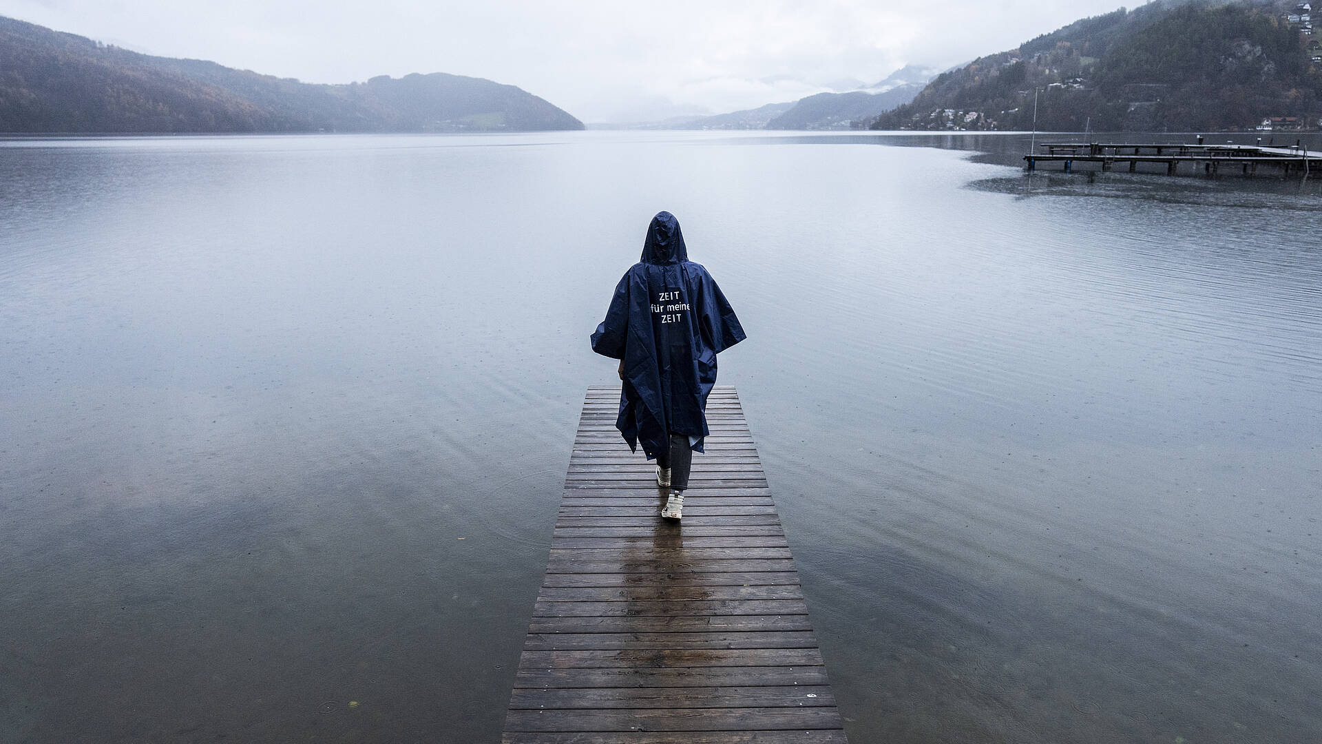 Person geht mit Regenponcho auf Steg