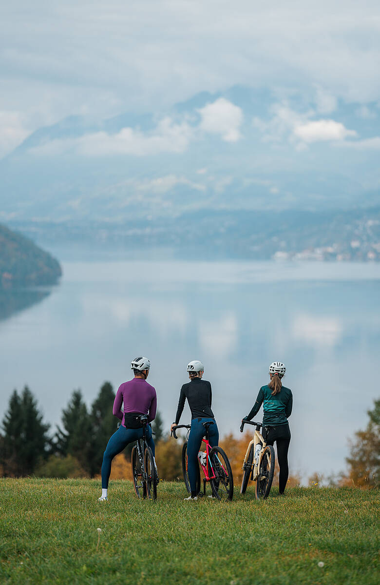 Drei Personen mit Fahrrädern auf Wiese oberhalb eines Sees