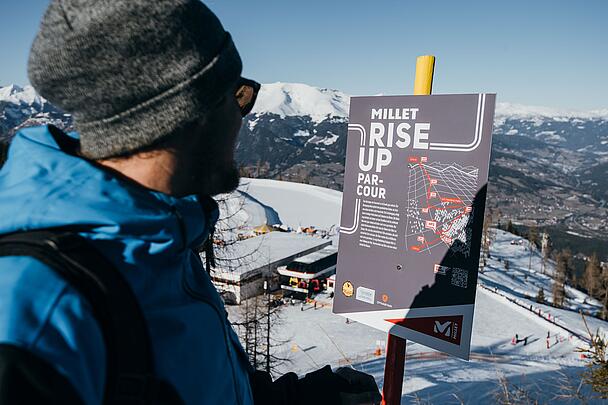 Skitourengeher blickt auf eine Tafel des Millet-Rise-Up Parcous