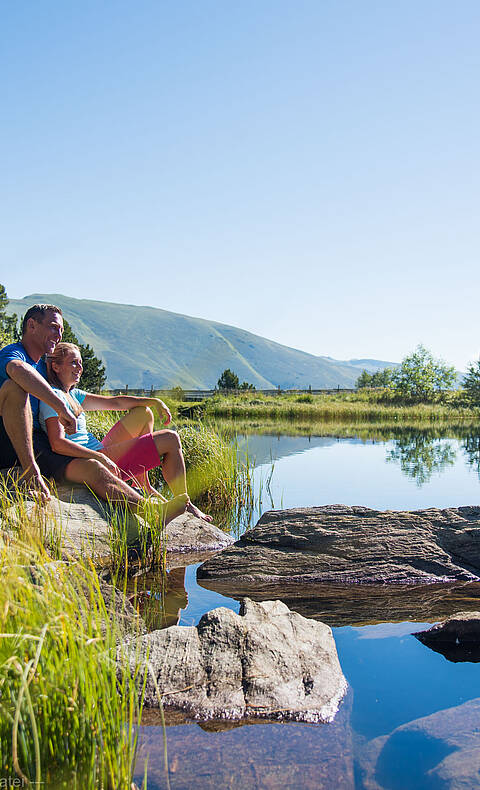 Pärchen sitzt in der Sonne am Ufer vom Windebensee auf der Nockalmstraße