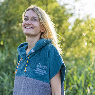 Junge Frau trägt Badeponcho in blau grau mit Logo auf der Brust
