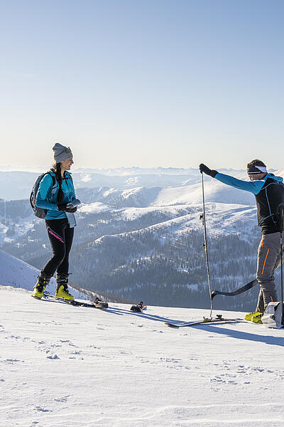 Ein Mann und eine Frau stehen in den Bergen und der Mann zieht gerade die Felle von seinen Tourenskiern ab