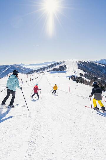 Familie fährt zusammen an einem sonnigen Tag eine Piste im Skigebiet Bad Kleinkirchheim hinunter