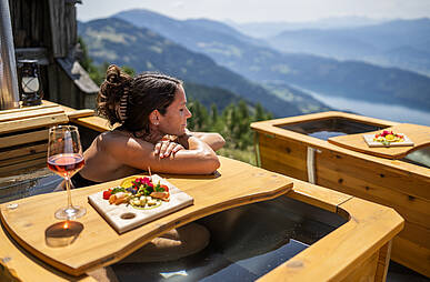 Frau entspannt in der Outdoor-Badewanne im AlmBad mit Blick auf den Millstätter See 