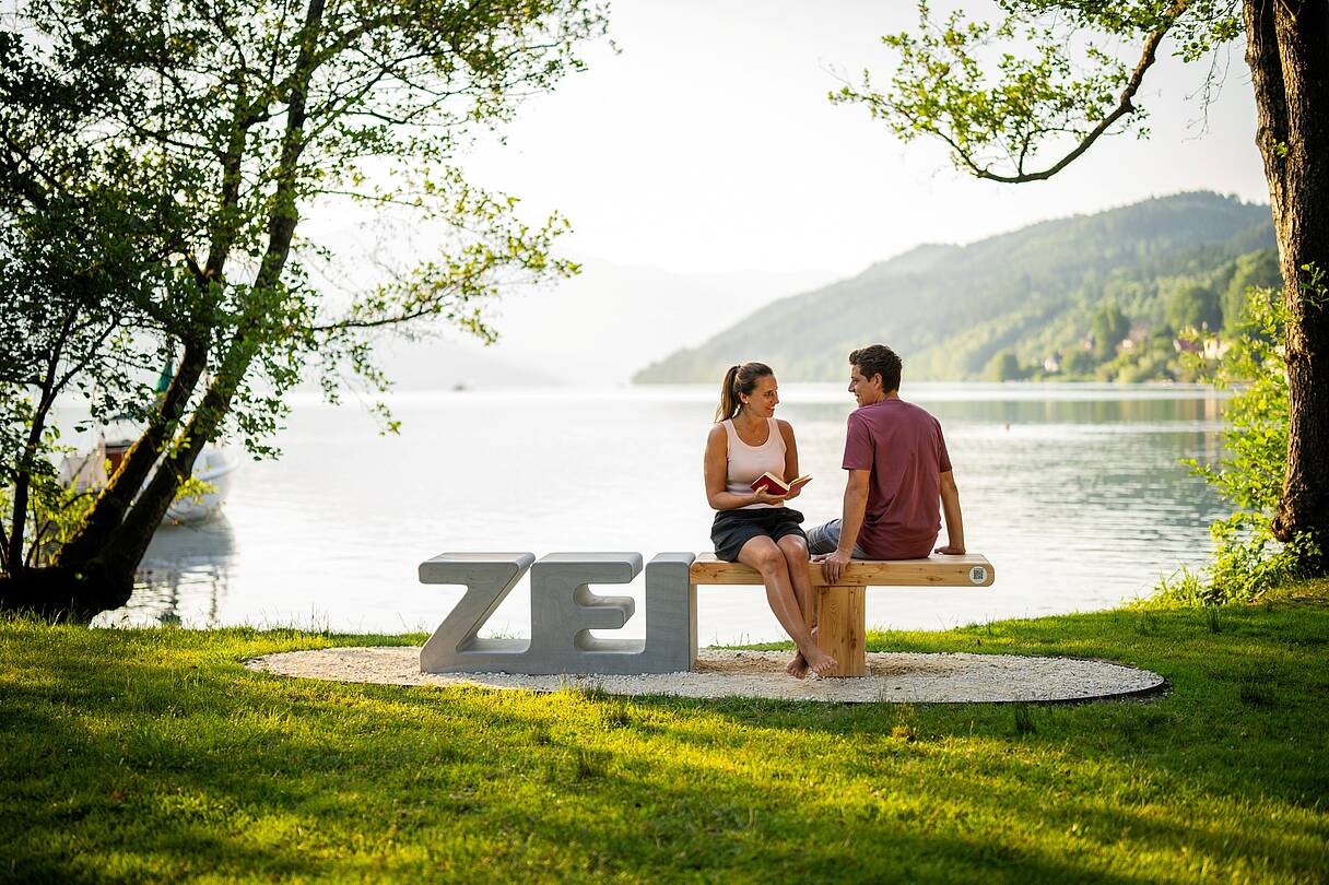 Pärchen sitzt auf Zeitbank mit dem Millstätter See im Hintergrund