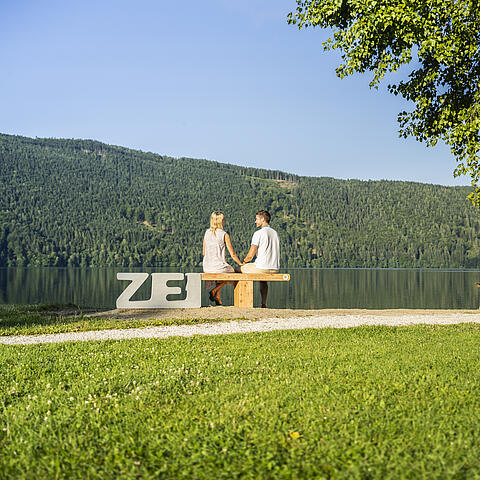 Pärchen sitzt auf ZEITbank und genießt das Millstätter See Panorama