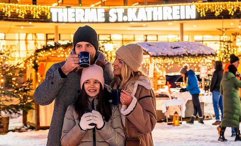 Glückliche Familie steht am Kirchheimer Adventmarkt und trinkt ein ein heißes Getränk