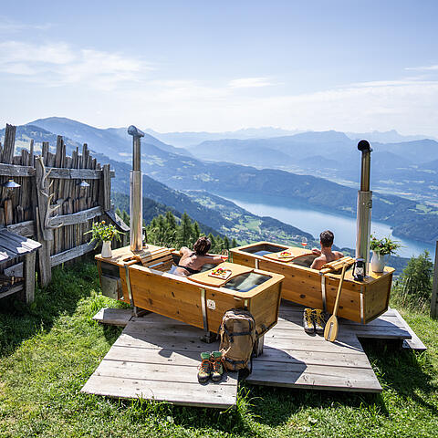 Ein Paar genießt ein AlmBad auf der AlexanderAlm mit Blick auf den Millstätter See.