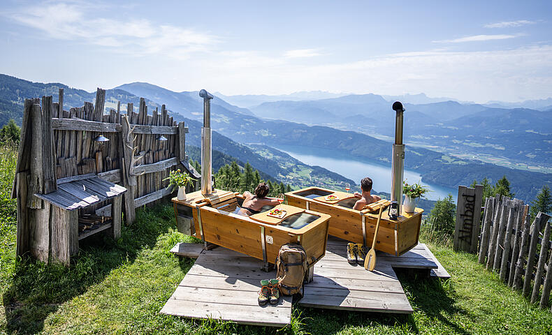 Ein Paar genießt ein AlmBad auf der AlexanderAlm mit Blick auf den Millstätter See.