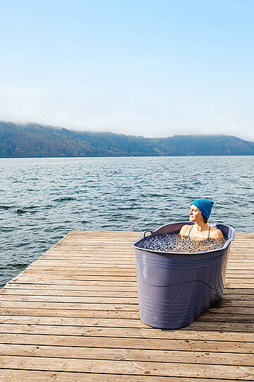 Frau liegt in Badewanne, die mit Eiswasser gefüllt ist, auf einem Holzsteg am Millstätter See