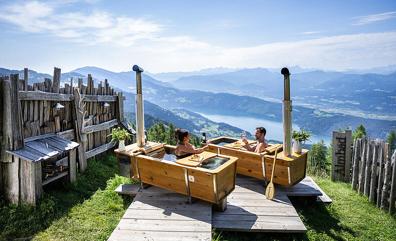 Zwei Personen genießen ein AlmBad in den Outdoorbadewannen auf der Alexanderalm, umgeben von unberührter Natur und Blick auf die Berge.