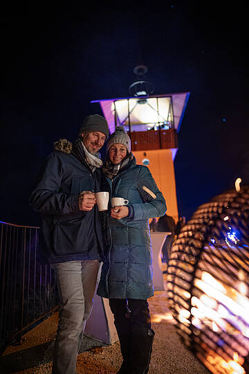 Pärchen mit heißen Getränken beim Feuer am Millstätter Lichtweg im Advent