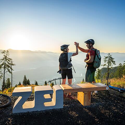 Gemeinsamen Gipfelsieg feiern am Sportberg Goldeck beim ZEITplatz 2 Personen feiern ihren Gipfelsieg am Goldeck beim Zeitplatz
