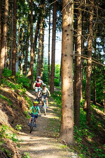 Eine Familie fährt mit Mountainbikes Trail in der Bike Area Obermillstatt hinunter